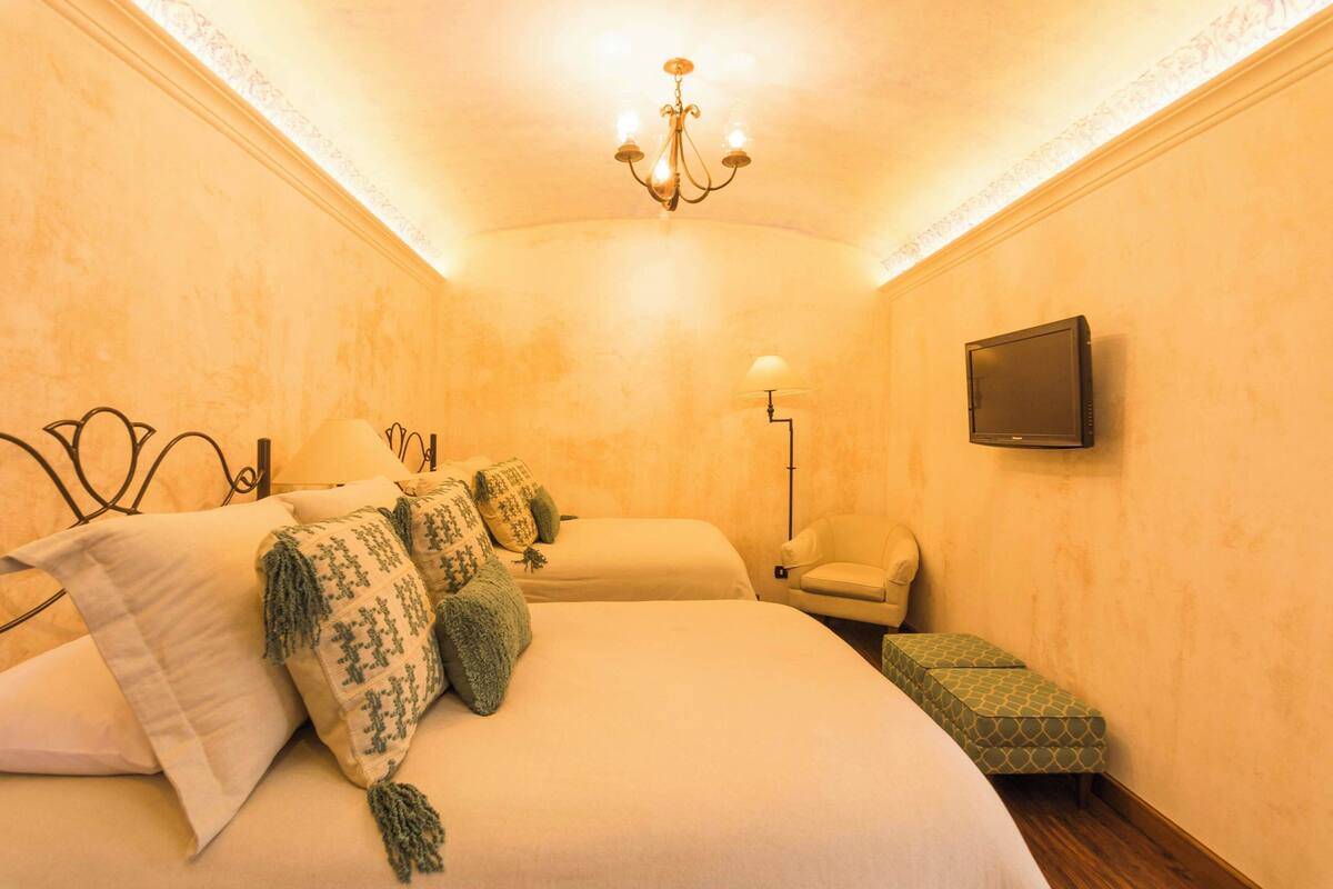 Ein Hotelzimmer mit einem großen Bett, einem Nachttisch, einem Sessel, einem Fernseher und einer Lampe.