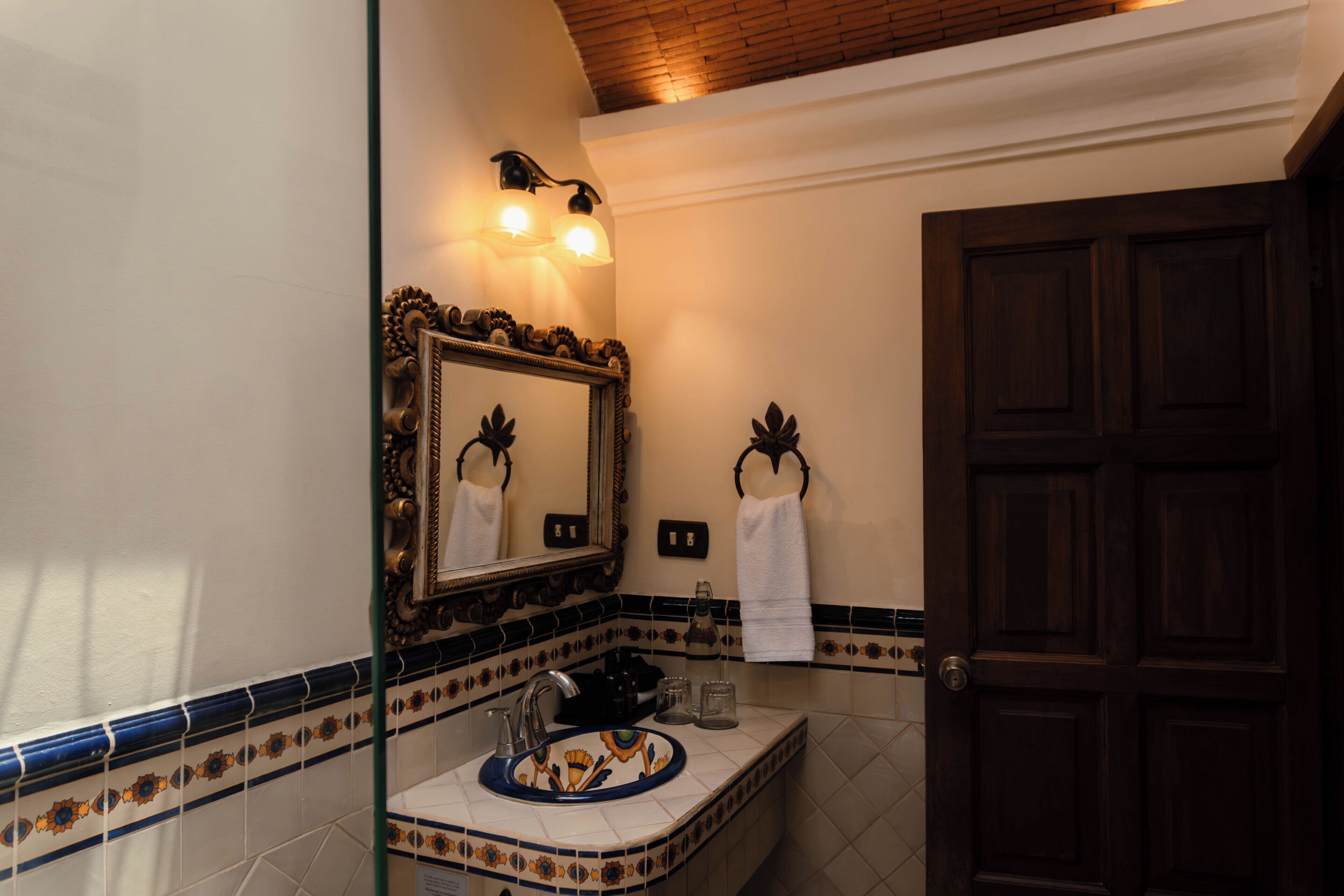 Un baño con un espejo grande, un lavabo con una pila decorativa, un perchero y una puerta.