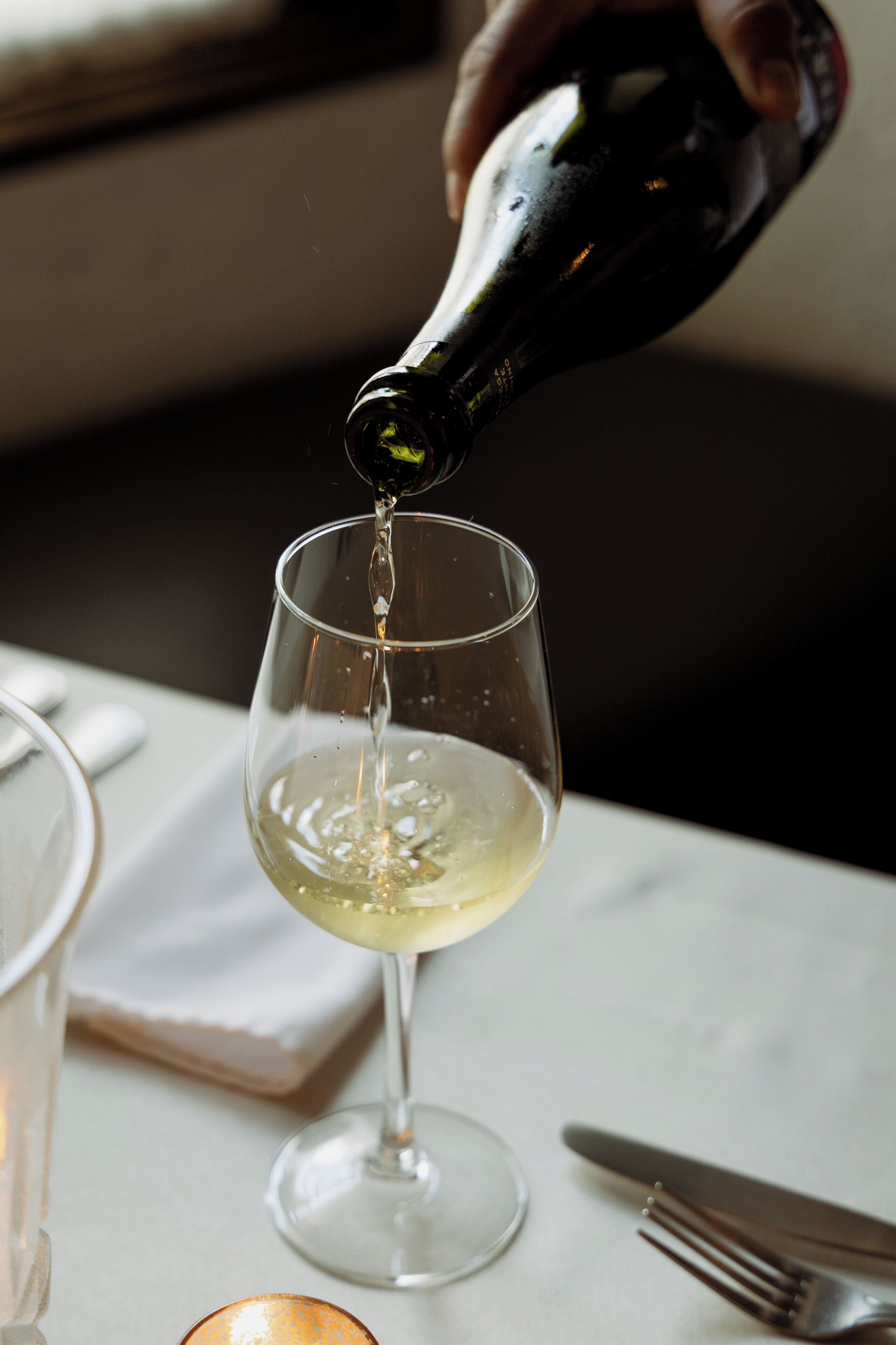 A hand pouring a clear liquid from a dark bottle into a wine glass.