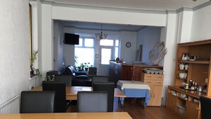 A dining area with a wooden table and chairs, a kitchen area with wooden cabinets and a countertop, and a living room with a sofa and a television. - The Address (Blackpool)