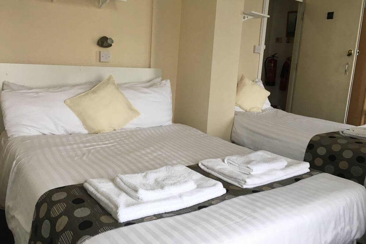 Habitación de hotel con dos camas, cada una con ropa blanca y una almohada. Hay toallas blancas dobladas sobre las camas.