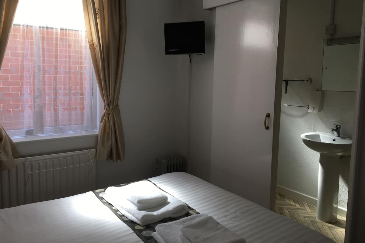 Una habitación de hotel con cama, televisión fijada en la pared, baño con lavabo y radiador.