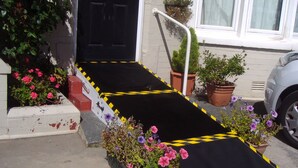 A black ramp leading to a black door with the number 93, flanked by potted plants and flowers. - The Address (Blackpool)