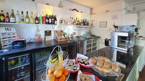 A bar area with shelves of liquor bottles, a refrigerator with beverages, and a display of pastries and fruits. - The Purple Tree Guest House (Torquay)