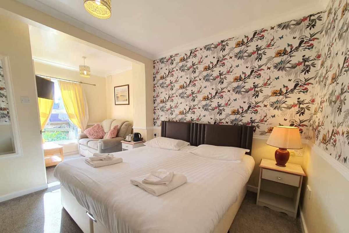 A hotel room with a large bed, a bedside table with a lamp, a chair, and a window with curtains.