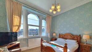 A bedroom with a large bed, a television, and a view of a cityscape through a window. - The Purple Tree Guest House (Torquay)