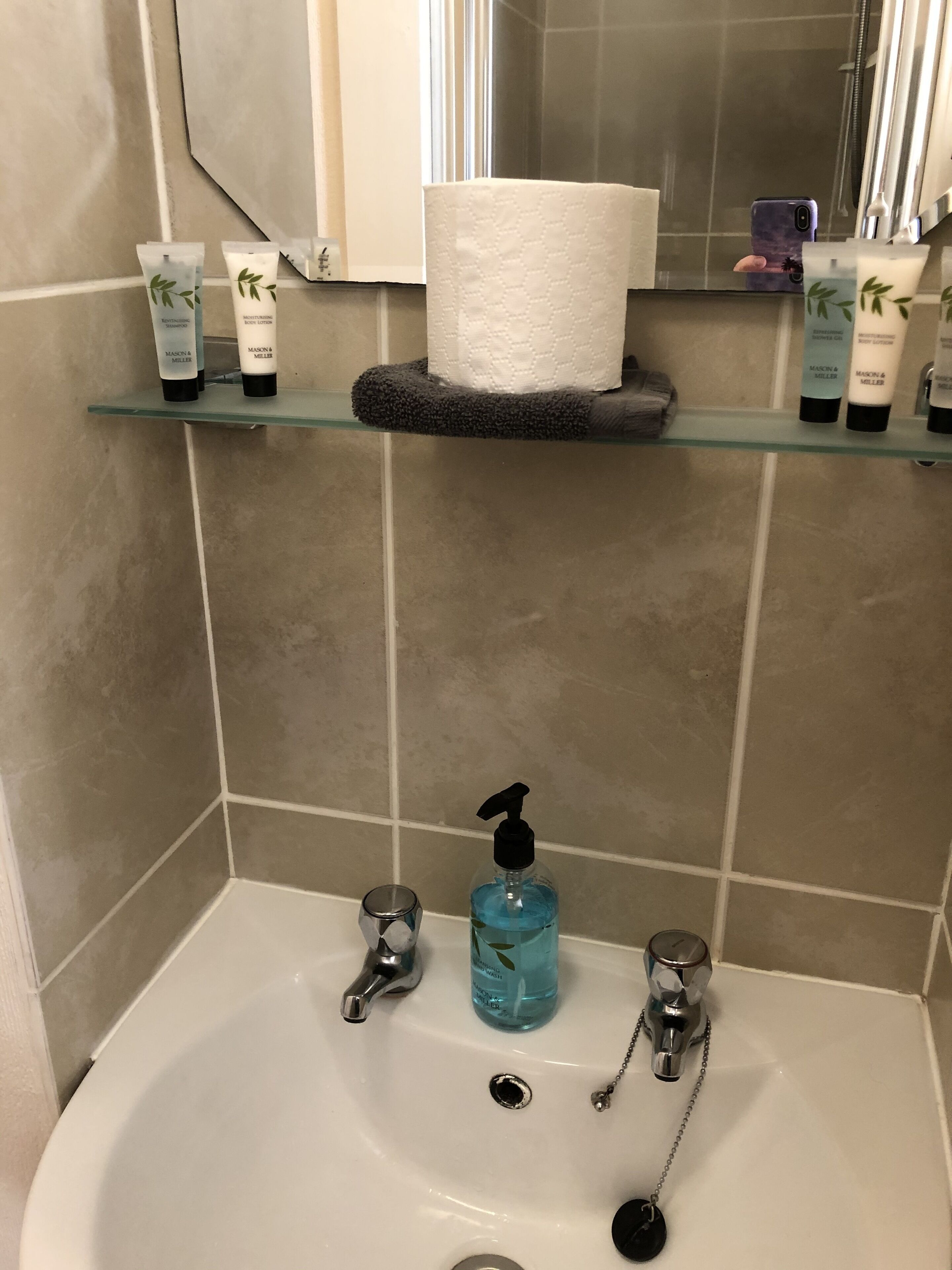 A bathroom with a white sink, two faucets, a soap dispenser, and a glass container.