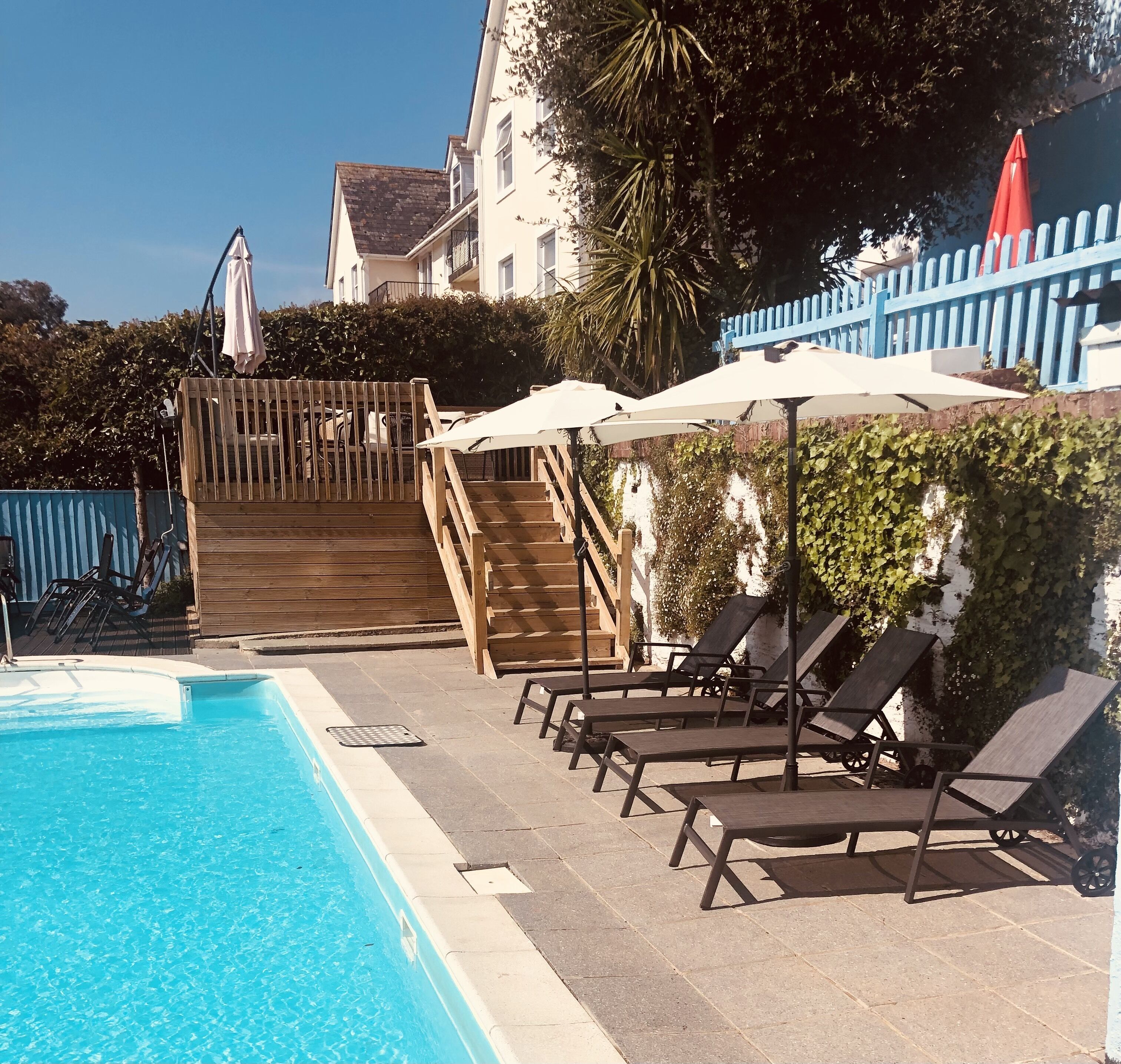 En swimmingpool med solstolar och parasoller, en trätrappa och ett staket.
