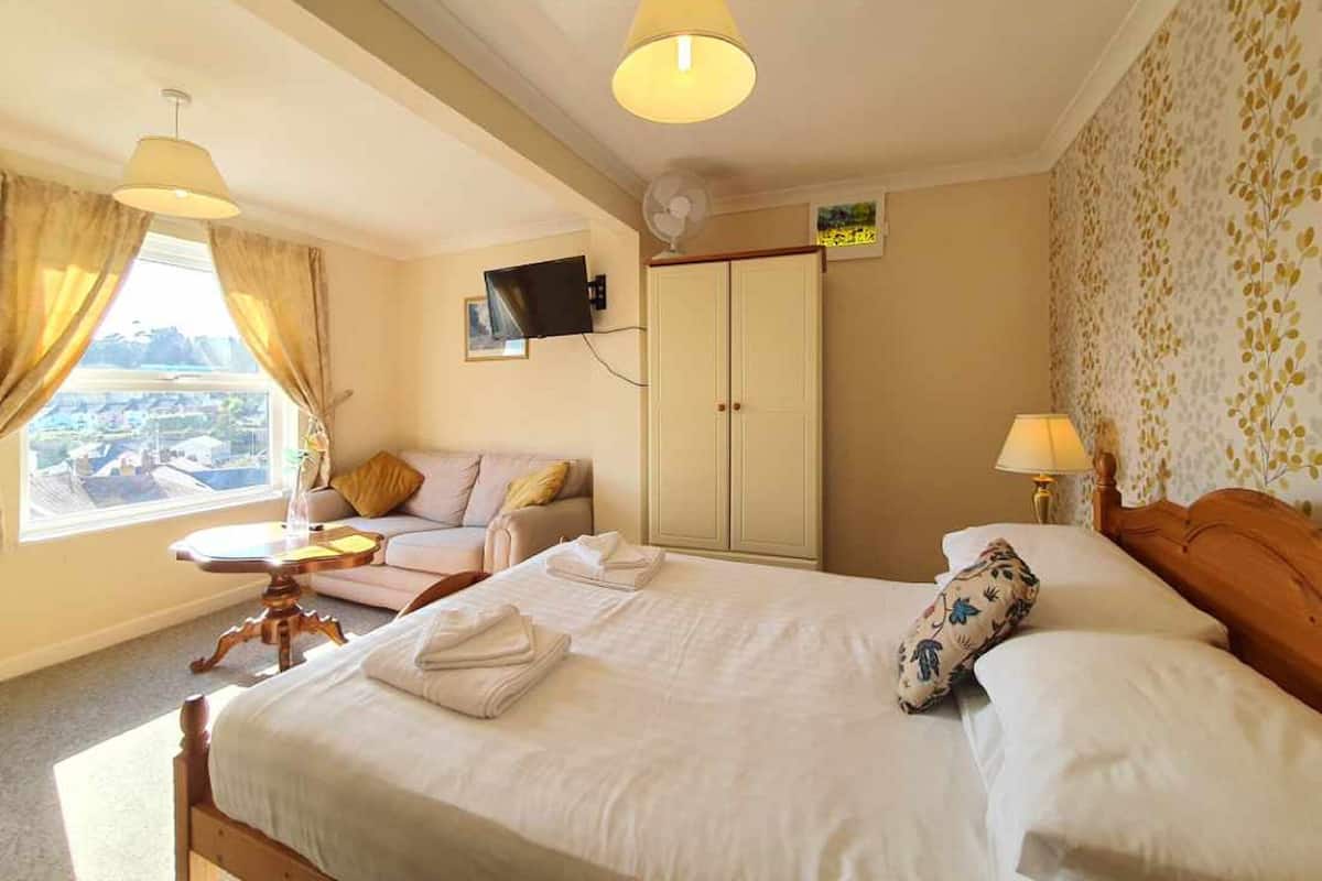 A hotel room with a bed, a desk, a wardrobe, a television, and a window with curtains.