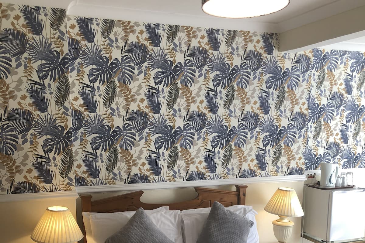 A neatly made bed with white linens, two bedside lamps, and a floral wallpaper pattern.
