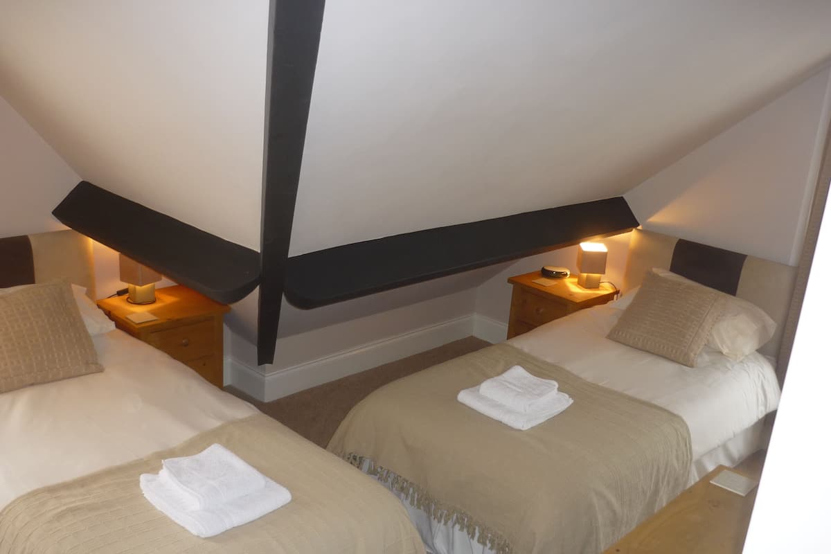 A room with two beds, each with a nightstand, a lamp, and a towel on the bed.