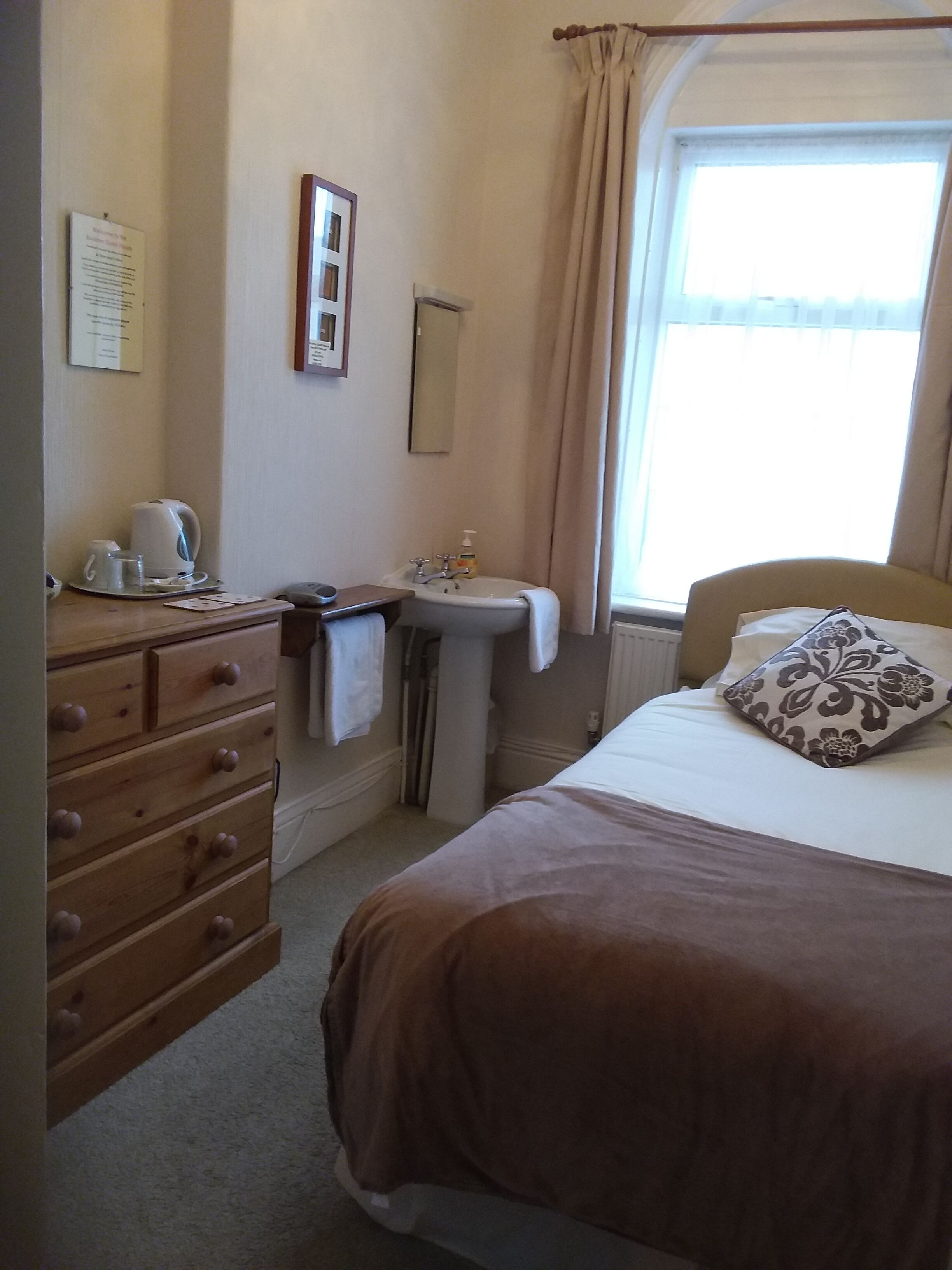 A hotel room with a bed, a dresser, a sink, and a window with curtains.