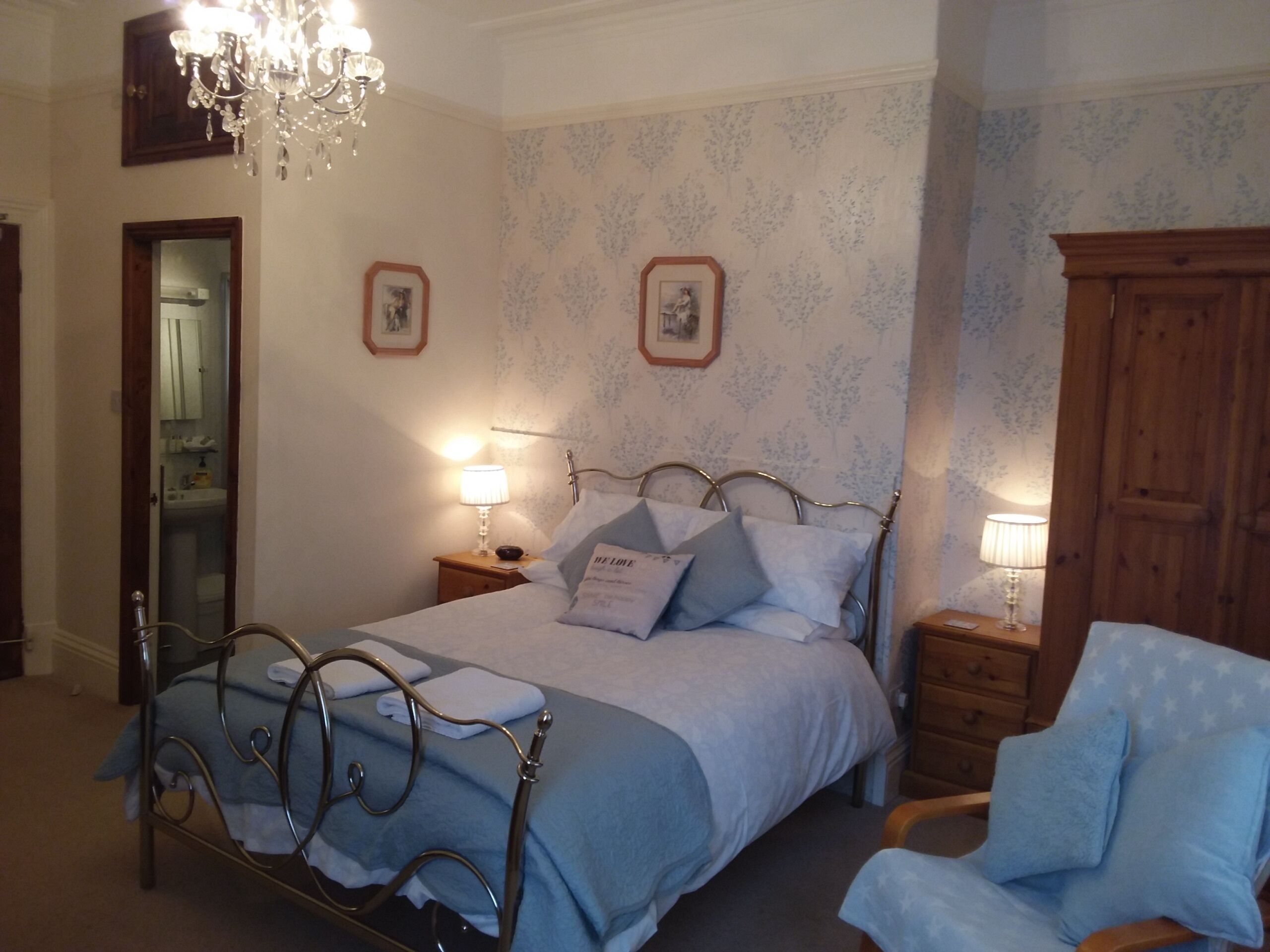 A bedroom with a metal bed frame, a wooden wardrobe, and a chandelier.