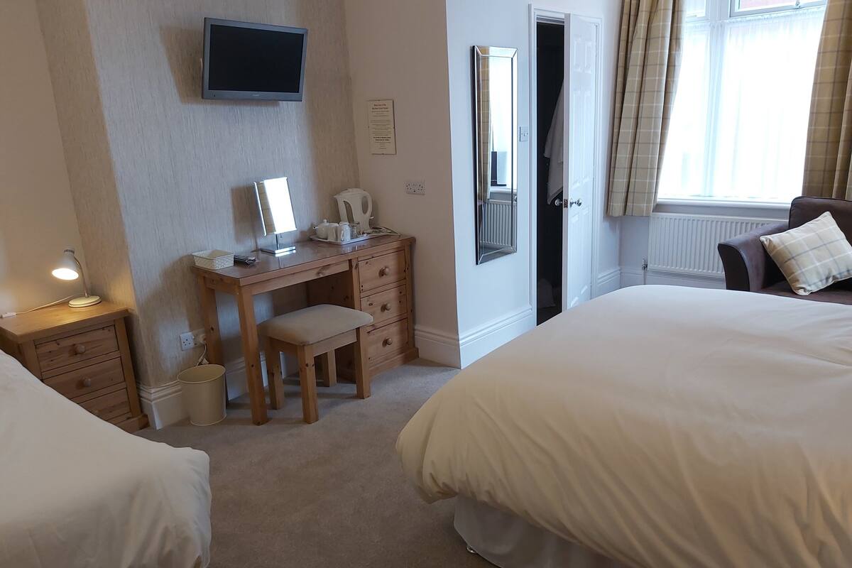 A hotel room with two beds, a desk with a chair, a television, and a mirror.