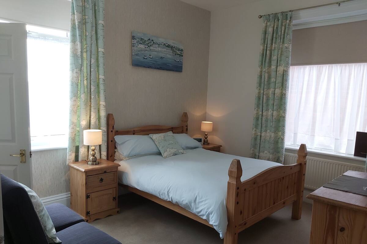 A bedroom with a wooden bed, two bedside tables with lamps, a chair, and a map-themed pillow.