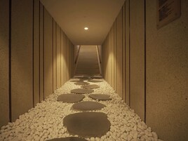 Un pasillo con un sendero de piedra y una escalera que sube a un nivel superior.