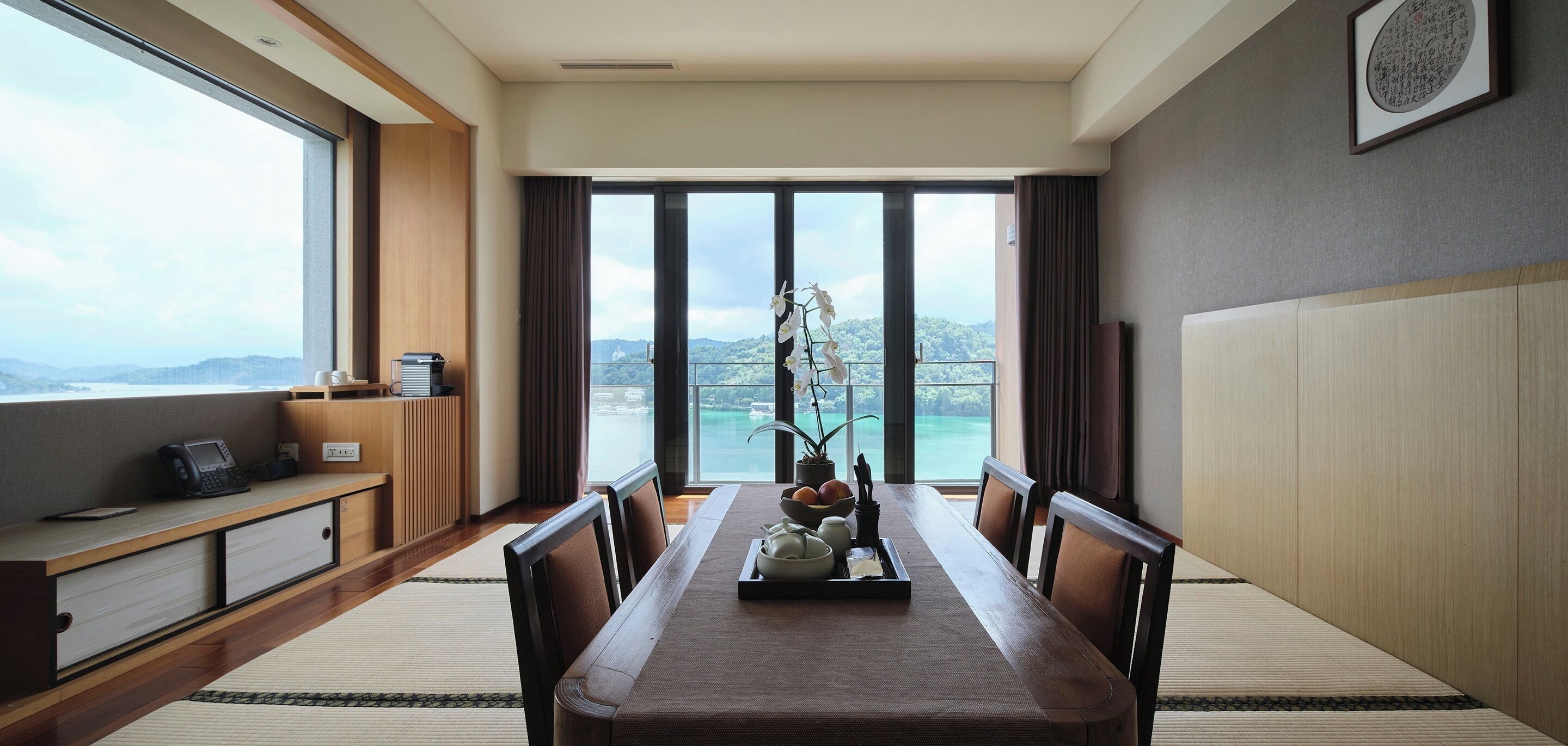 Un comedor moderno con una mesa grande, sillas y vistas a una masa de agua a través de amplios ventanales.