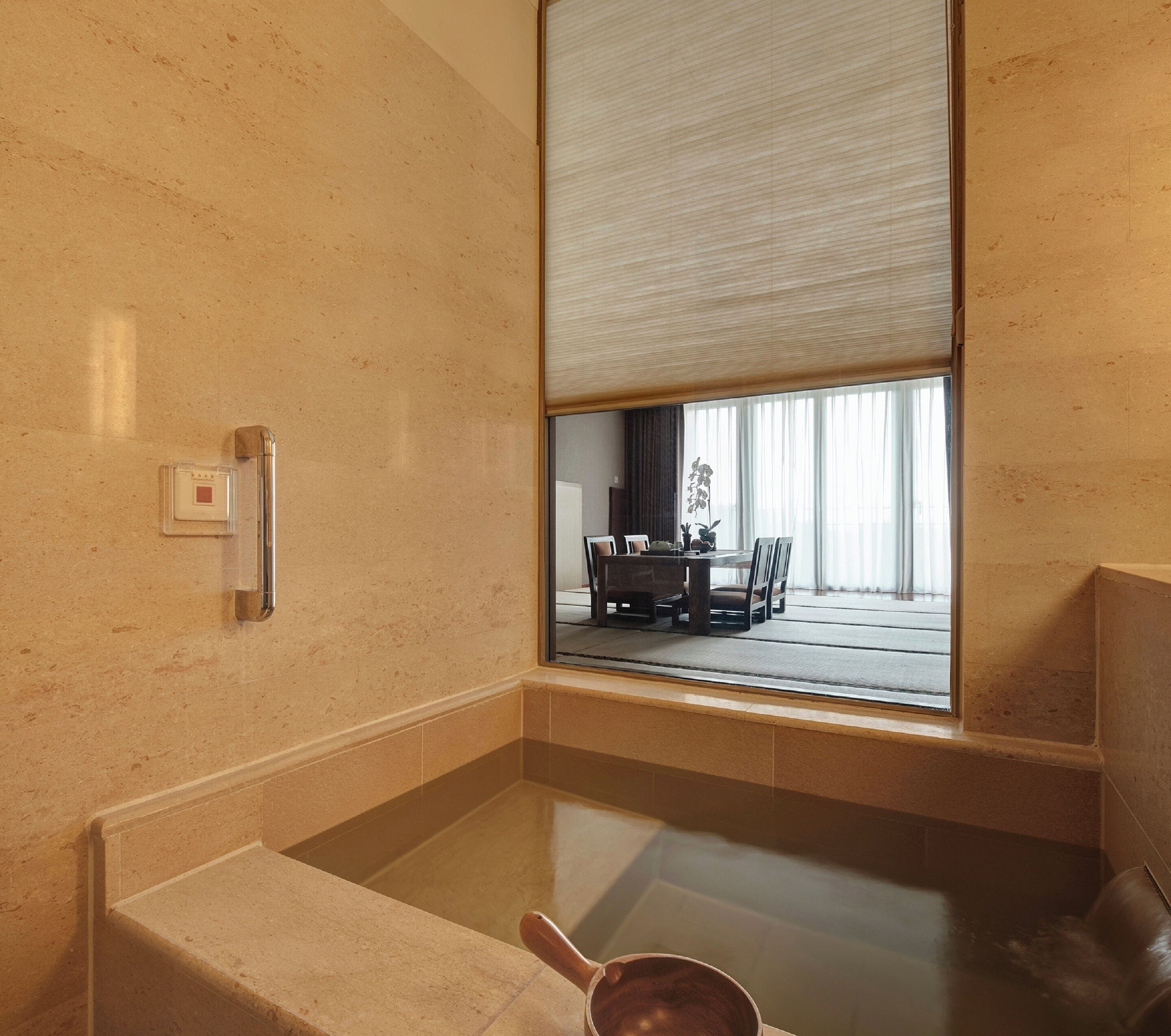 A modern bathroom with a bathtub, a shower, and a toilet. There is a window with a view of a dining area.