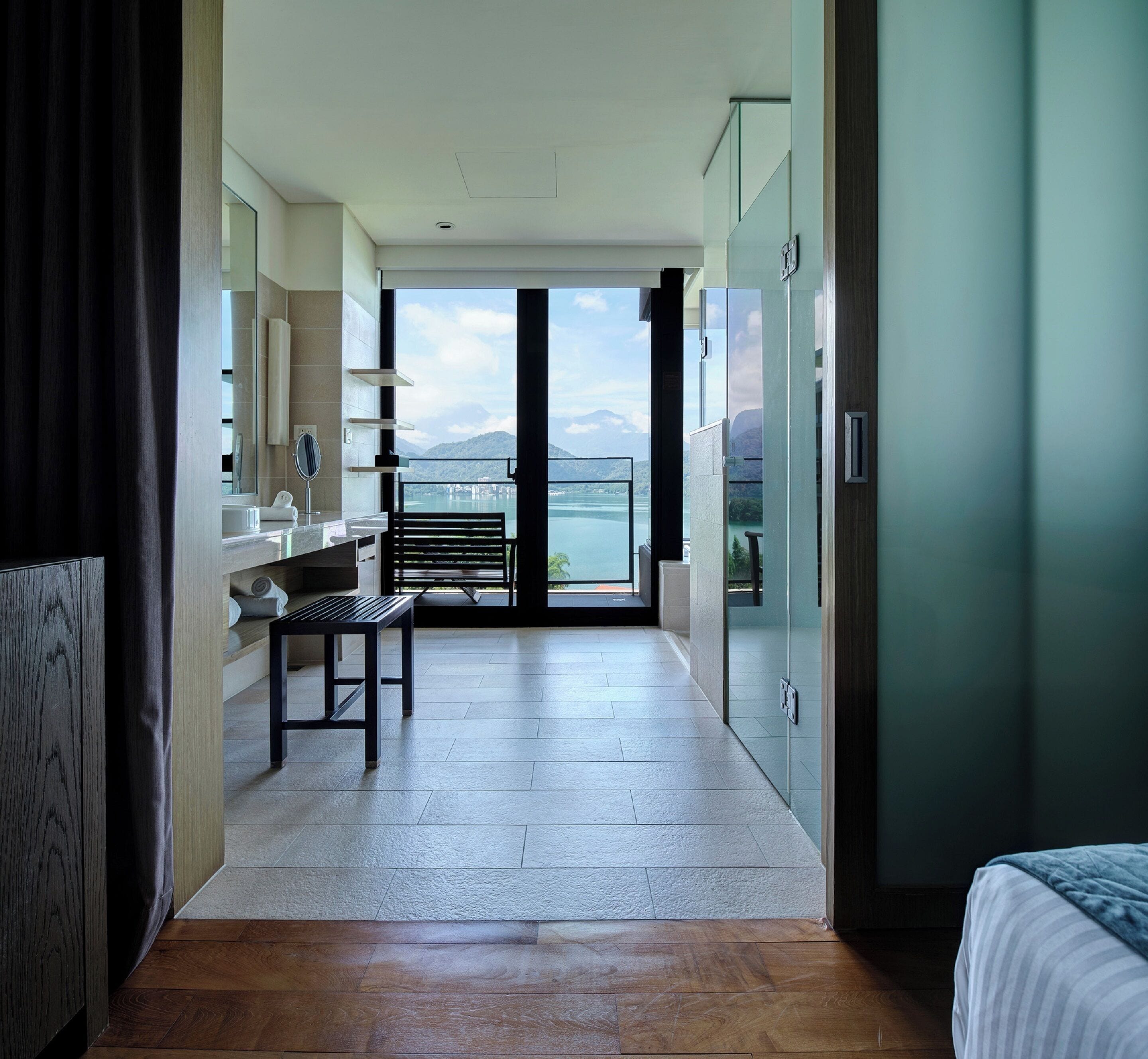 Et moderne hotelværelse med et stort vindue, der giver en smuk udsigt over bjerge og en sø.