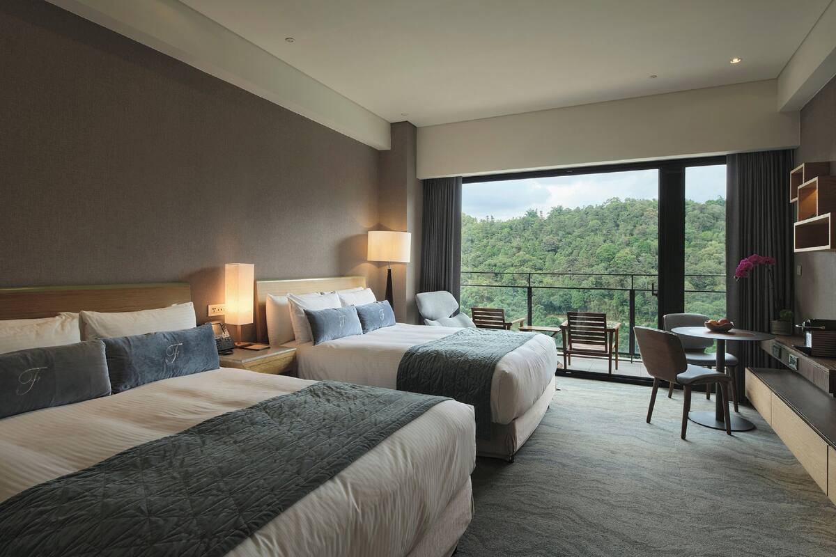 Habitación de hotel con dos camas, un escritorio y un balcón con vistas al bosque.