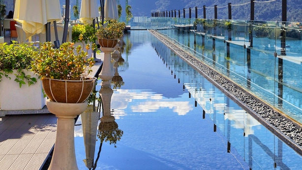 Uma piscina longa e reflexiva com plantas em vasos e guarda-sóis, com vista para uma cordilheira.