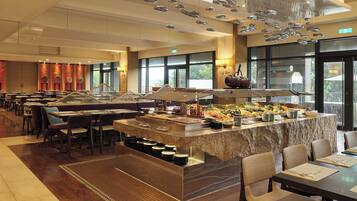 Un comedor amplio con varias mesas y sillas, una barra de buffet con diversos alimentos, y un ventanal que ofrece vistas al exterior.