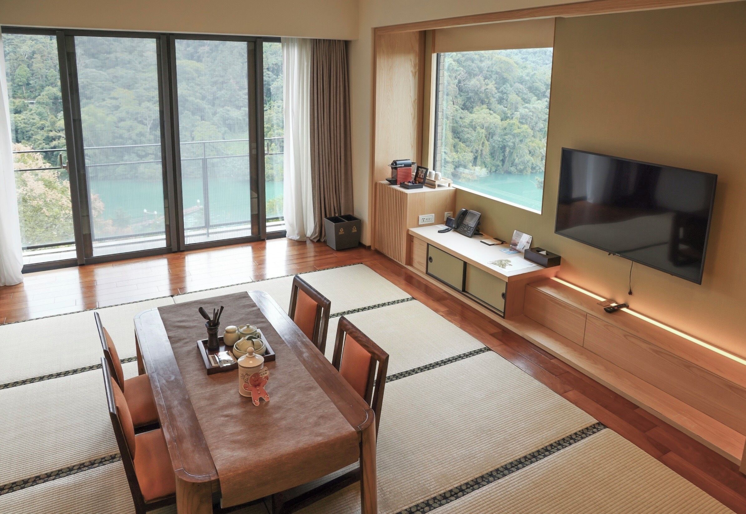 Ein modernes Zimmer mit einem Holzespeisetisch, Tatami-Matten, einem Fernseher und einem Balkon mit schöner Aussicht.
