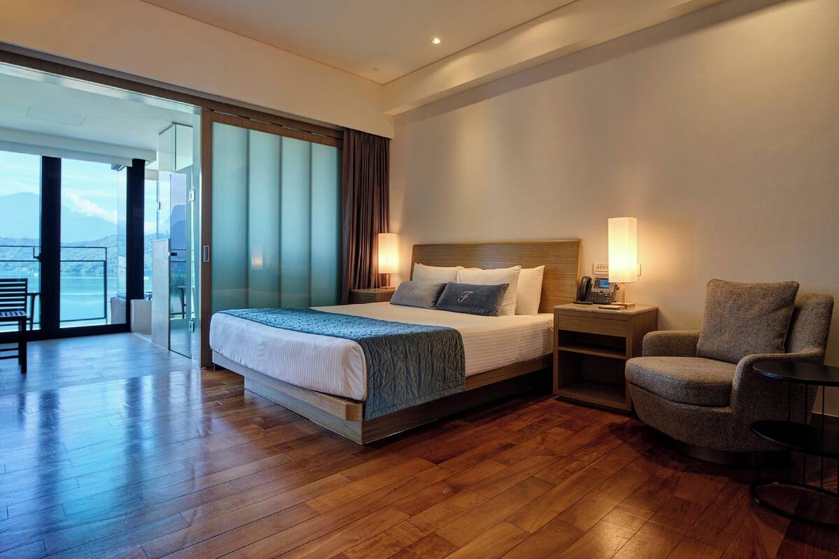 Una habitación de hotel moderna con una cama grande, una silla, una mesita de noche y vistas al exterior.