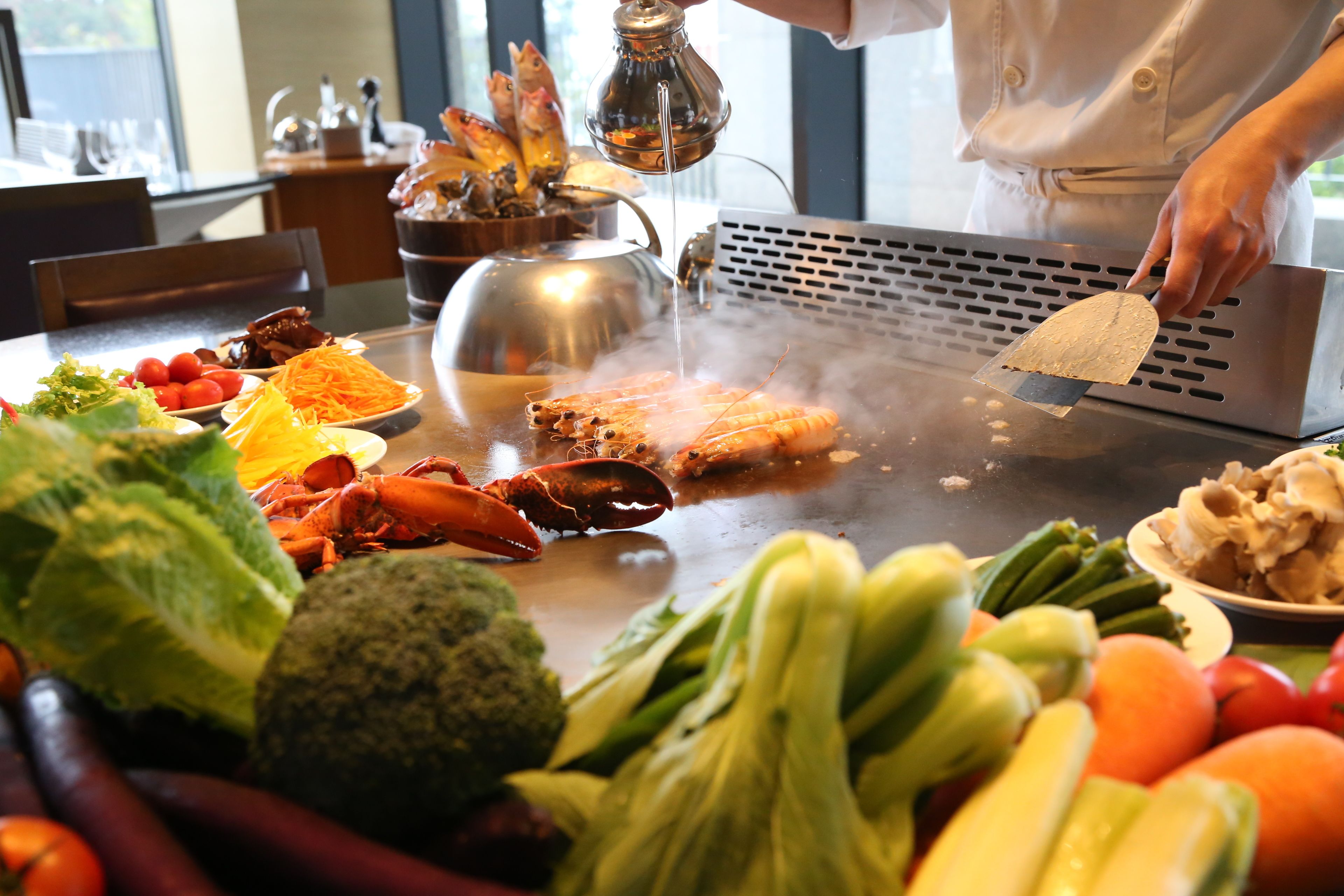 Un chef preparando mariscos a la parrilla junto a una variedad de verduras y mariscos.