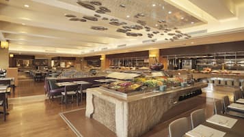 A spacious hotel lobby with a central buffet area, multiple seating arrangements, and a modern ceiling design.