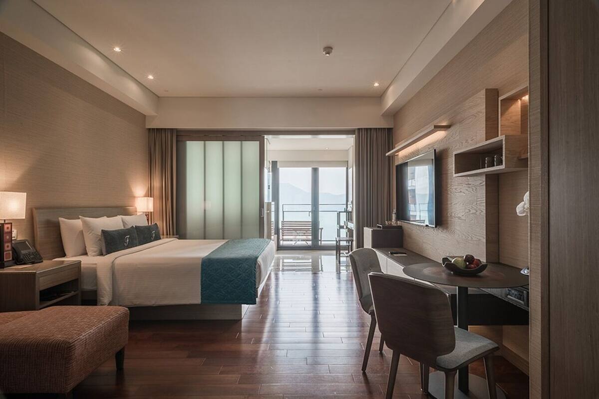 Habitación de hotel con cama, escritorio, sillas, televisor y vista al exterior.