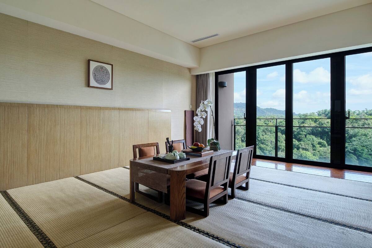 Un comedor con mesa de madera, sillas y vistas a un bosque a través de amplios ventanales.