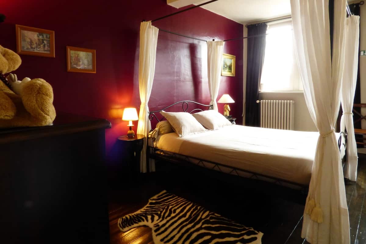 A bedroom with a bed, two bedside lamps, a zebra-patterned rug, a teddy bear, and a radiator.