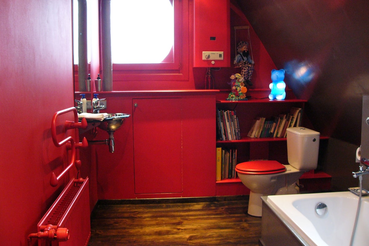 A red bathroom with a window, a sink, a toilet, and a bathtub.