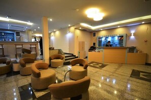Un vestíbulo de hotel con una recepción, una zona de bar y varias opciones de asientos.