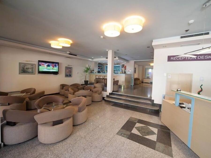 A hotel lobby with a reception desk, sofas, a television, and a staircase leading to other areas.