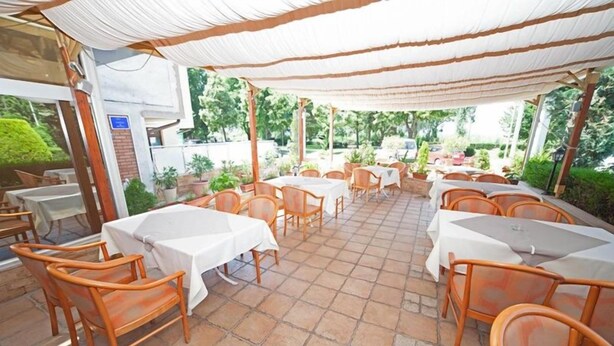 An outdoor patio area with multiple tables and chairs, covered by a white canopy. - Lebed (Ohrid)