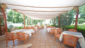 An outdoor dining area with tables and chairs under a canopy, surrounded by greenery. - Lebed (Ohrid)