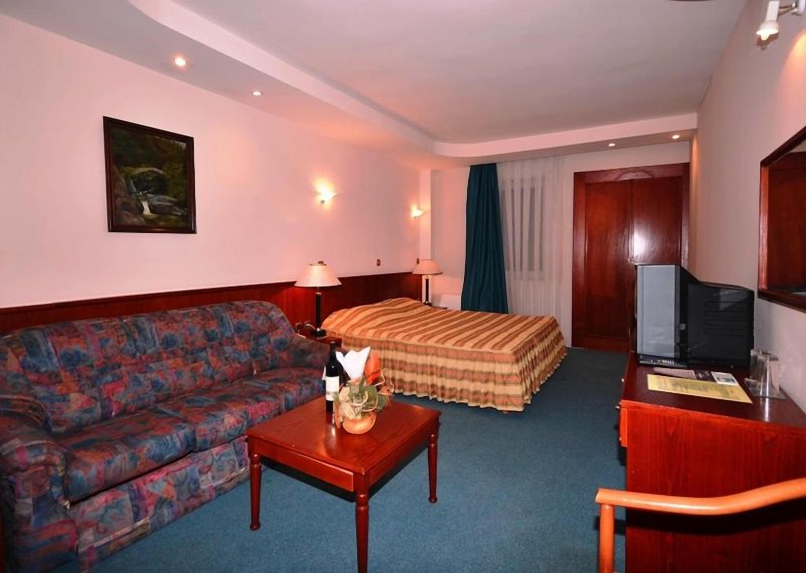 A hotel room with a sofa, a bed, a desk, and a television.