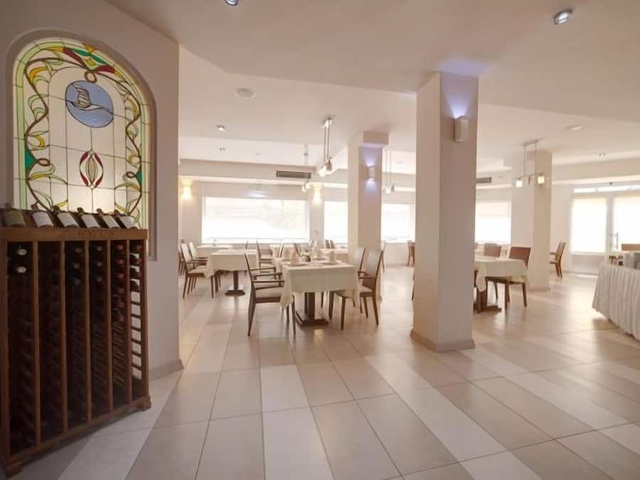 A spacious dining area with multiple tables and chairs, a stained glass window, and a wine rack.