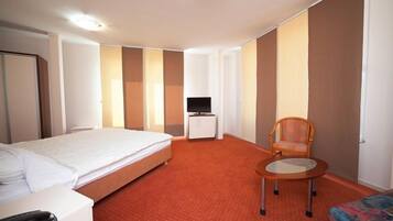 A hotel room with a bed, a small table, a chair, a television, and a wardrobe.