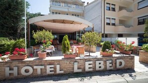 A hotel named "HOTEL LEBED" with an outdoor seating area, potted plants, and a covered patio.
