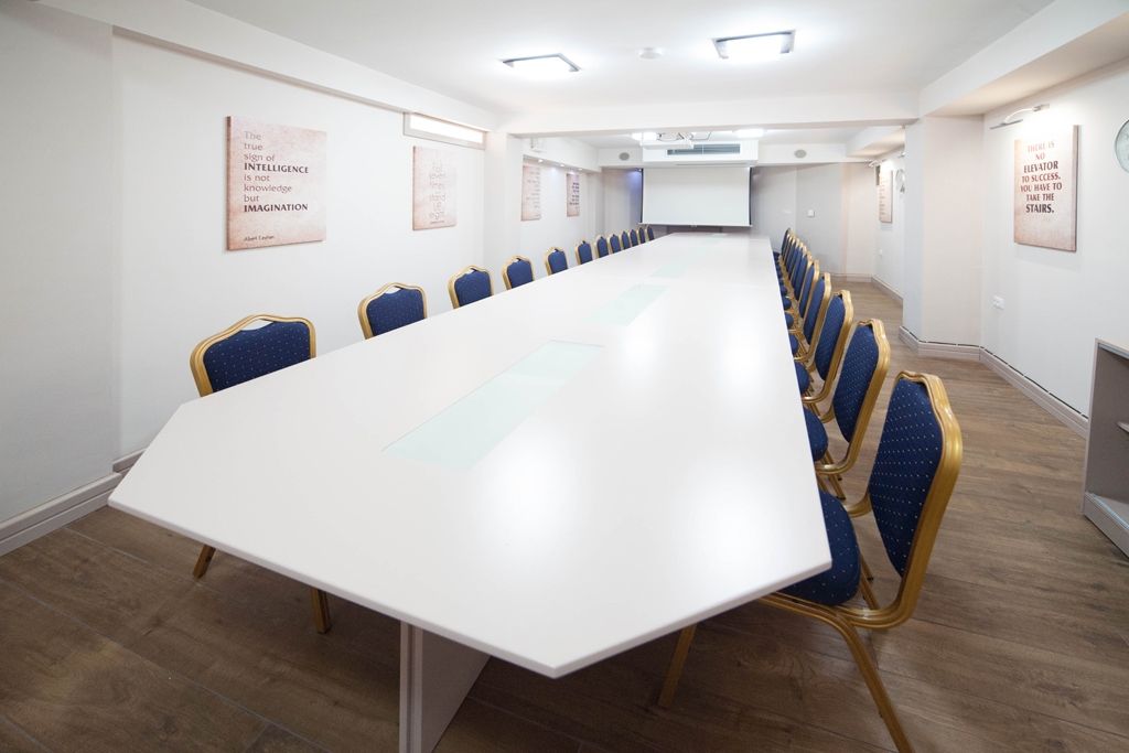 A conference room with a long white table, blue upholstered chairs, and motivational posters on the walls.