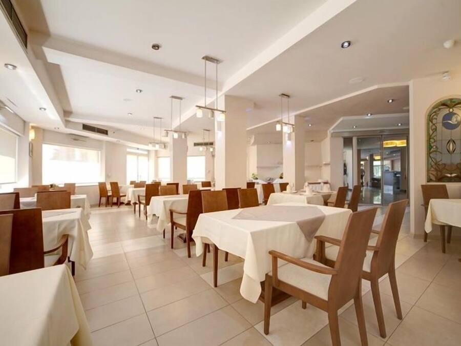 Zona pranzo con diversi tavoli e sedie disposti in file, caratterizzata da soffitto alto e illuminazione a incasso.