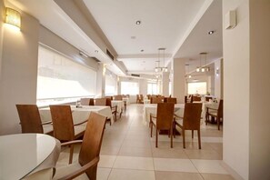 Un comedor moderno con mesas y sillas redondas, ventanas amplias e iluminación empotrada.