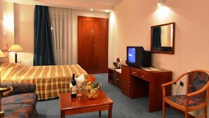 A hotel room with a sofa, a small table with a bottle and glasses, a desk with a computer, a chair, and a TV. - Lebed (Ohrid)
