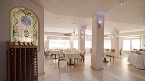 A spacious dining area with multiple tables and chairs, a stained glass window, and a wine rack.