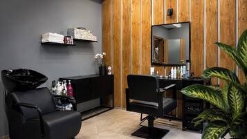 Un salón moderno con dos sillas de peluquería negras, un panel de pared de madera, un espejo y una estantería con productos para el cabello.