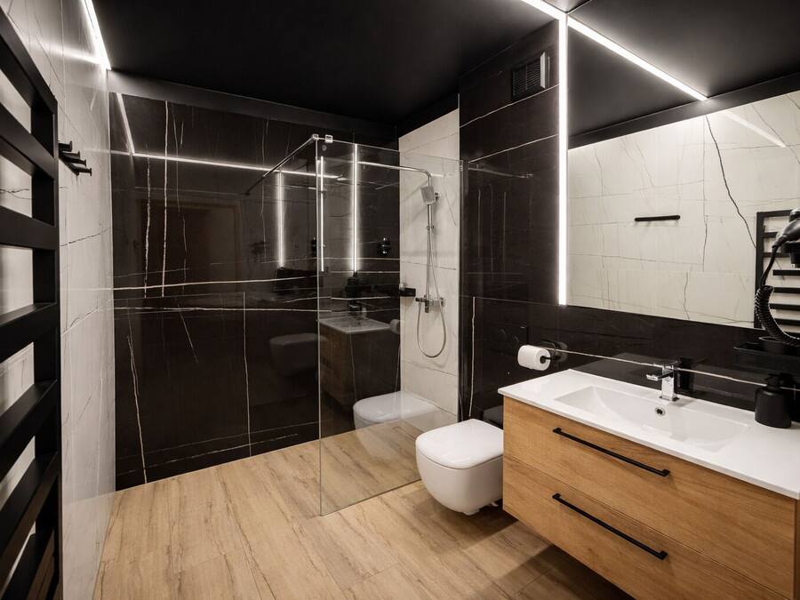 A modern bathroom with a glass shower enclosure, a white toilet, a wooden vanity with a sink, and a large mirror.