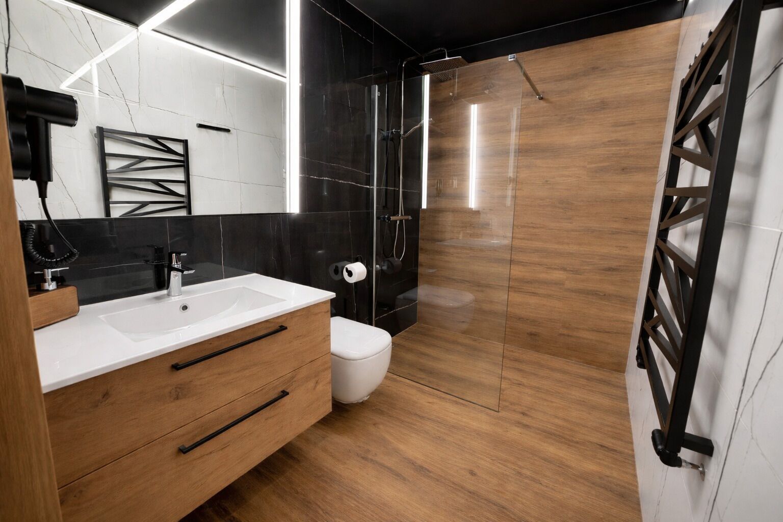 A modern bathroom with a wooden vanity, a glass shower enclosure, and a black and white tiled wall.